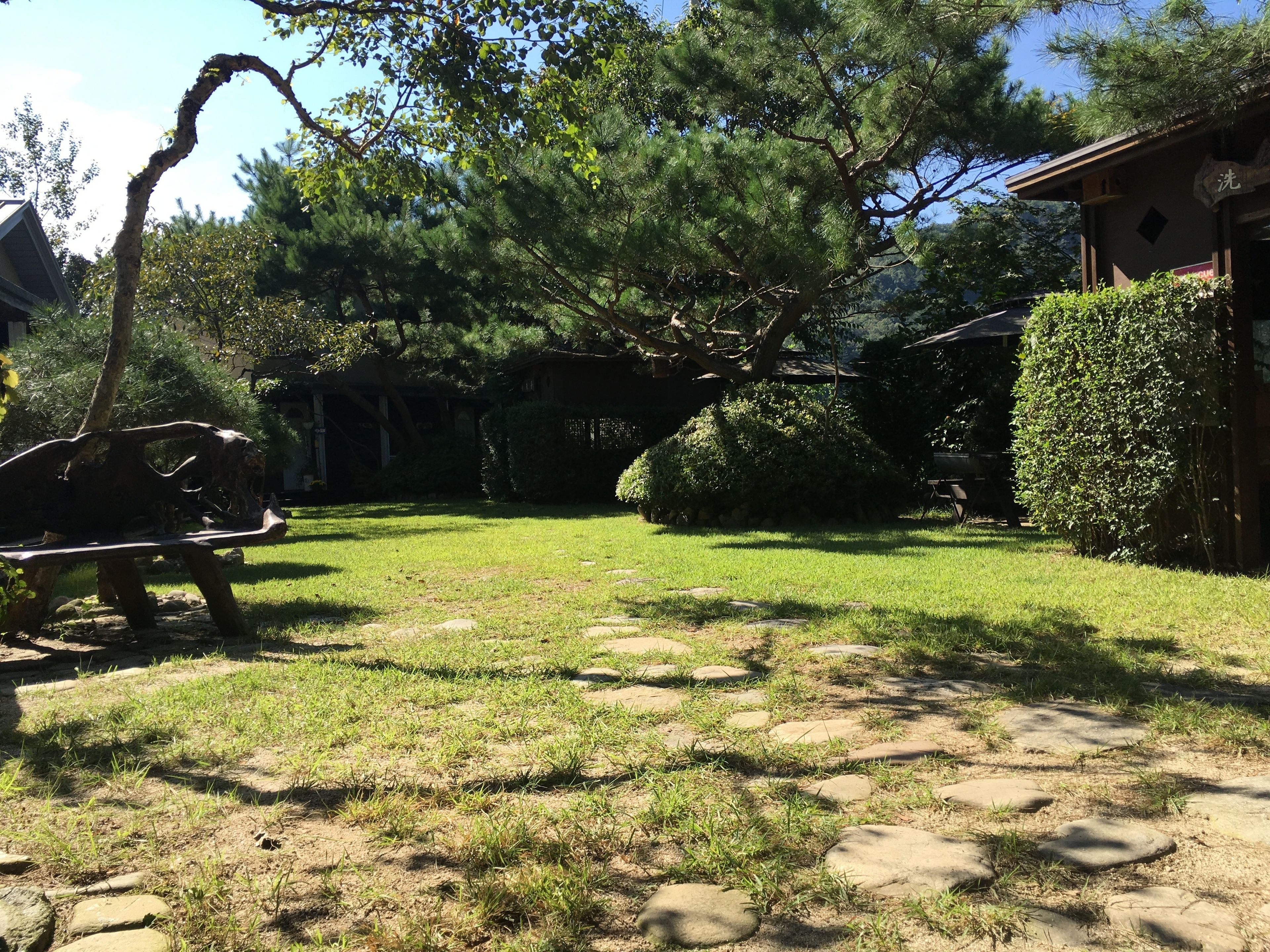 A garden with a stone pathway, a wooden bench, and a building with a sign.