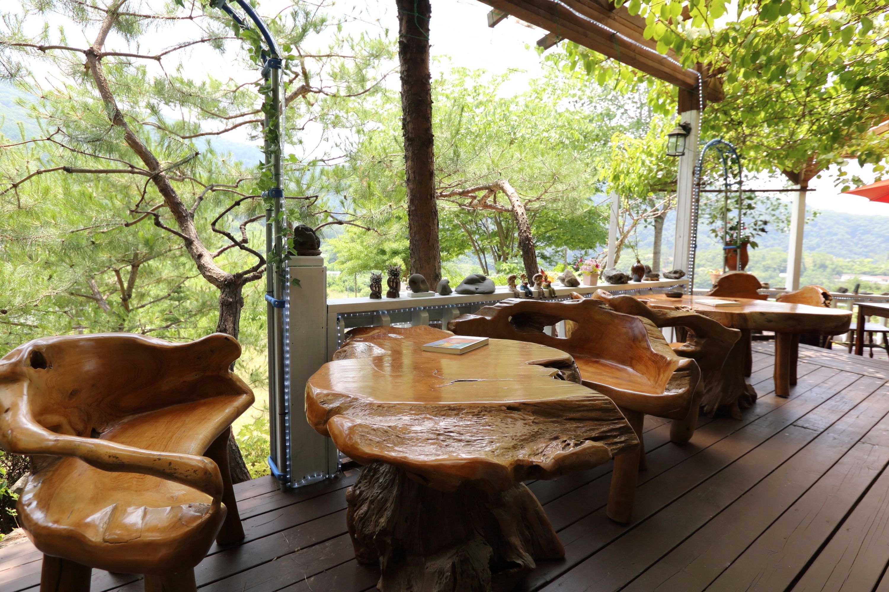 A wooden deck with rustic furniture, including chairs and a table, surrounded by trees and a view of the mountains.
