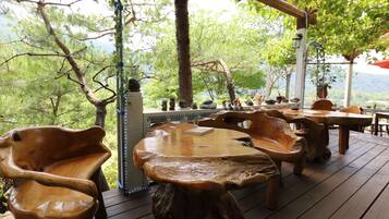 A wooden deck with rustic furniture, including chairs and a table, surrounded by trees and a view of the mountains.