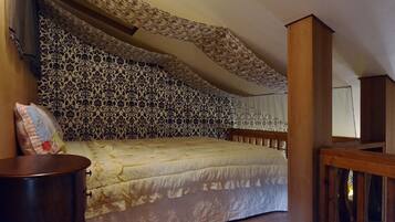 Un dormitorio con papel tapiz estampado, una cama con cubrecama floral, cabecera de madera y mesita de noche con lámpara.