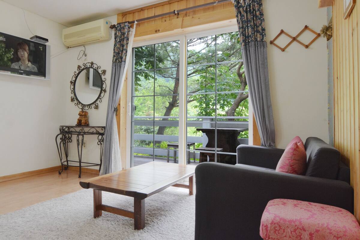 A living room with a sofa, a coffee table, a TV, and a large window with curtains.
