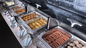 Buffet com diversas opções de comida, incluindo ovos, salsichas e pães.