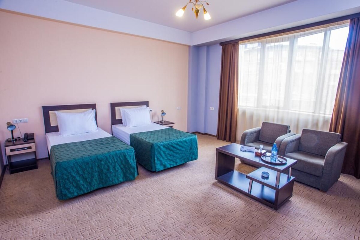 A hotel room with two single beds, a sofa, a coffee table, and a large window with curtains.
