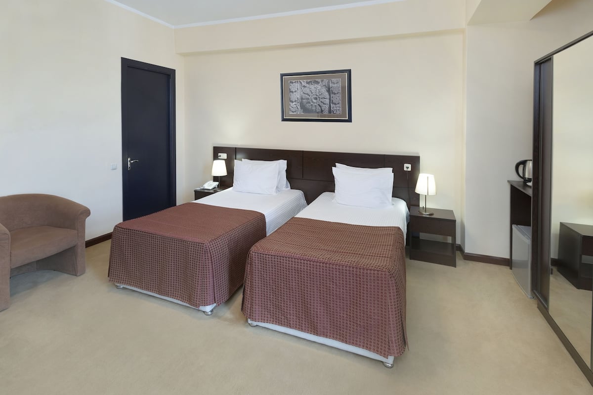 Habitación de hotel con dos camas, un escritorio, una silla y un cuadro en la pared.