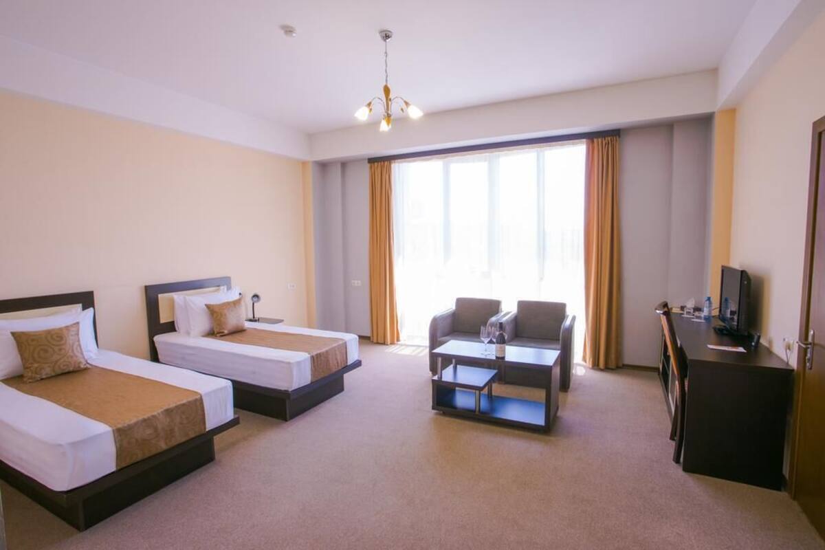Habitación de hotel con dos camas individuales, un sofá, una mesa de centro, un televisor y un escritorio.