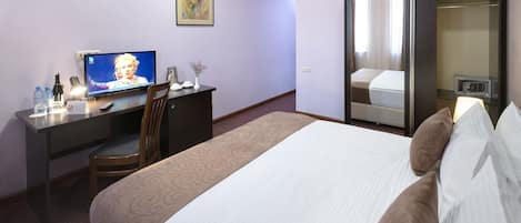 Habitación de hotel con cama, escritorio con televisor, silla, armario y una pequeña mesa con un jarrón.