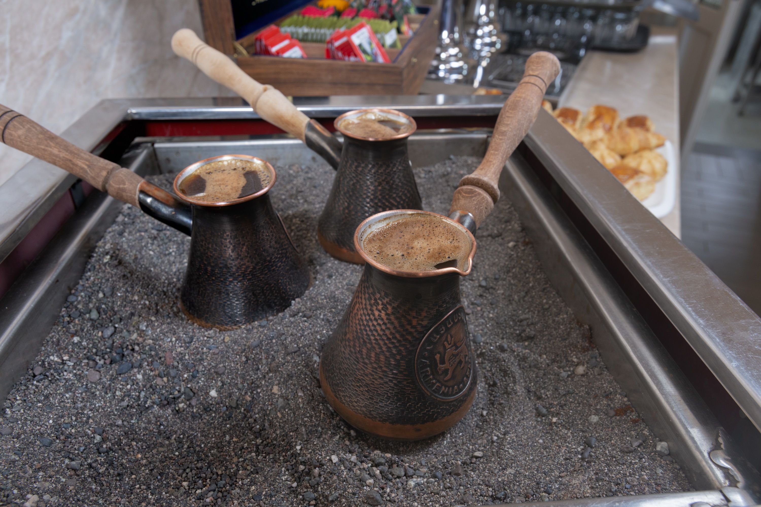 Zwei traditionelle Kaffeekannen auf einer Schale mit Holzgriff, platziert auf einer Oberfläche mit strukturierter Musterung.