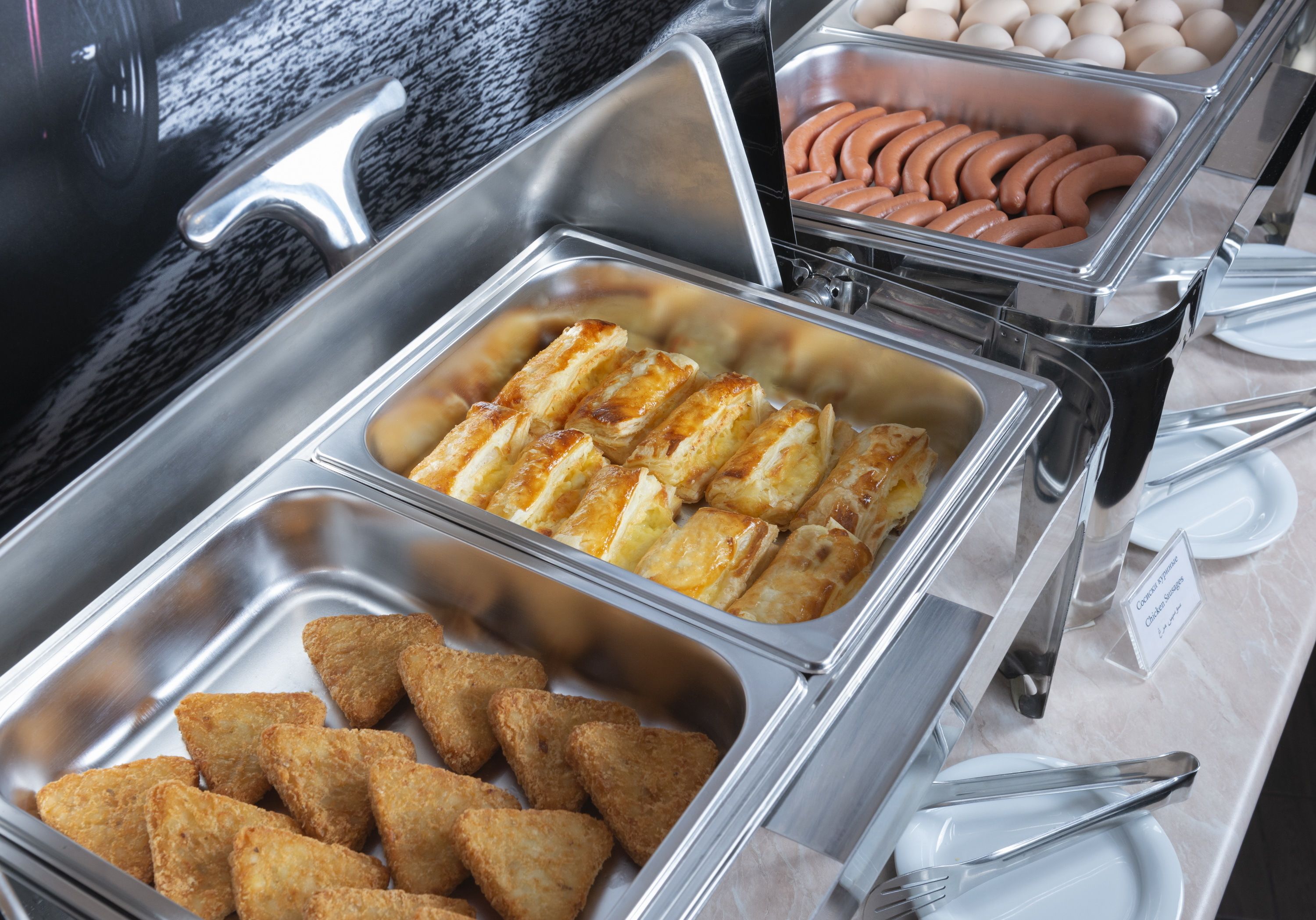 Un buffet proposant une variété d’aliments, notamment du pain, des œufs et des saucisses.
