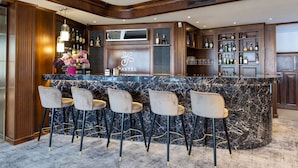 A bar area with a marble countertop, four bar stools, and a variety of bottles and glasses on shelves. - Hotel Meridian (Cluj-Napoca)