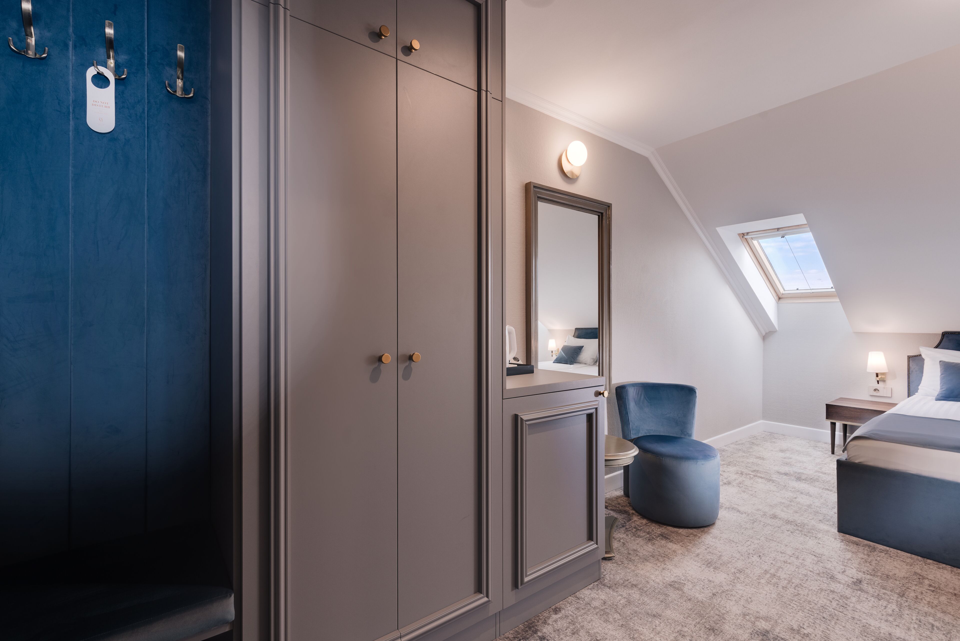 A bedroom with a large wardrobe, a mirror, a round ottoman, a bed, and a skylight.