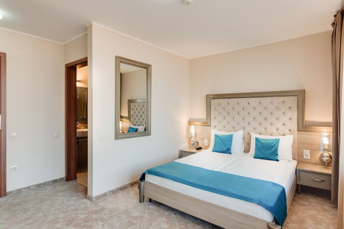 Habitación de hotel con una cama grande, un espejo, lámparas de noche y una puerta que da a un baño.