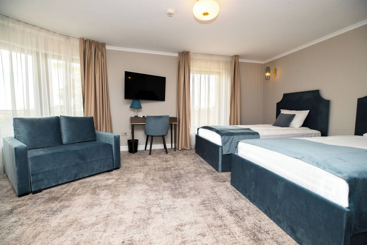 Habitación de hotel con sofá, dos camas individuales, escritorio con silla y televisión en la pared.