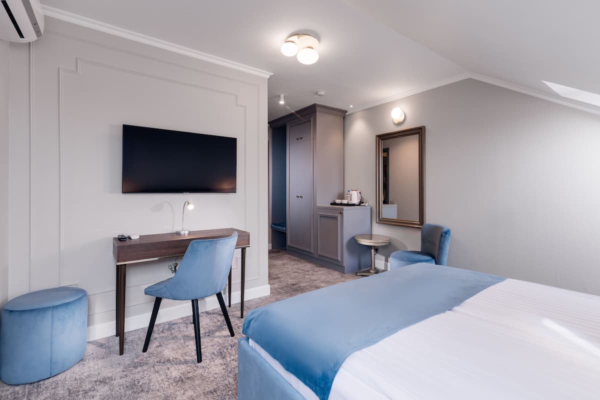 Habitación de hotel con cama, escritorio, silla, televisor, espejo y una pequeña mesa.