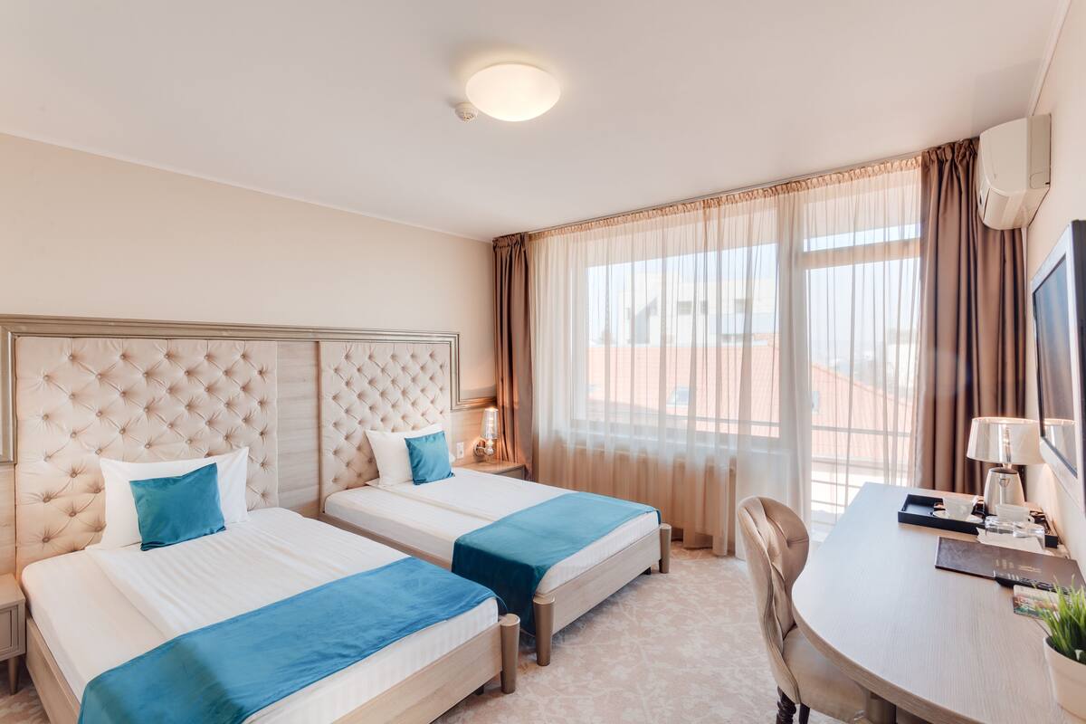 Una habitación de hotel con dos camas, un escritorio, una silla y un ventanal con cortinas.
