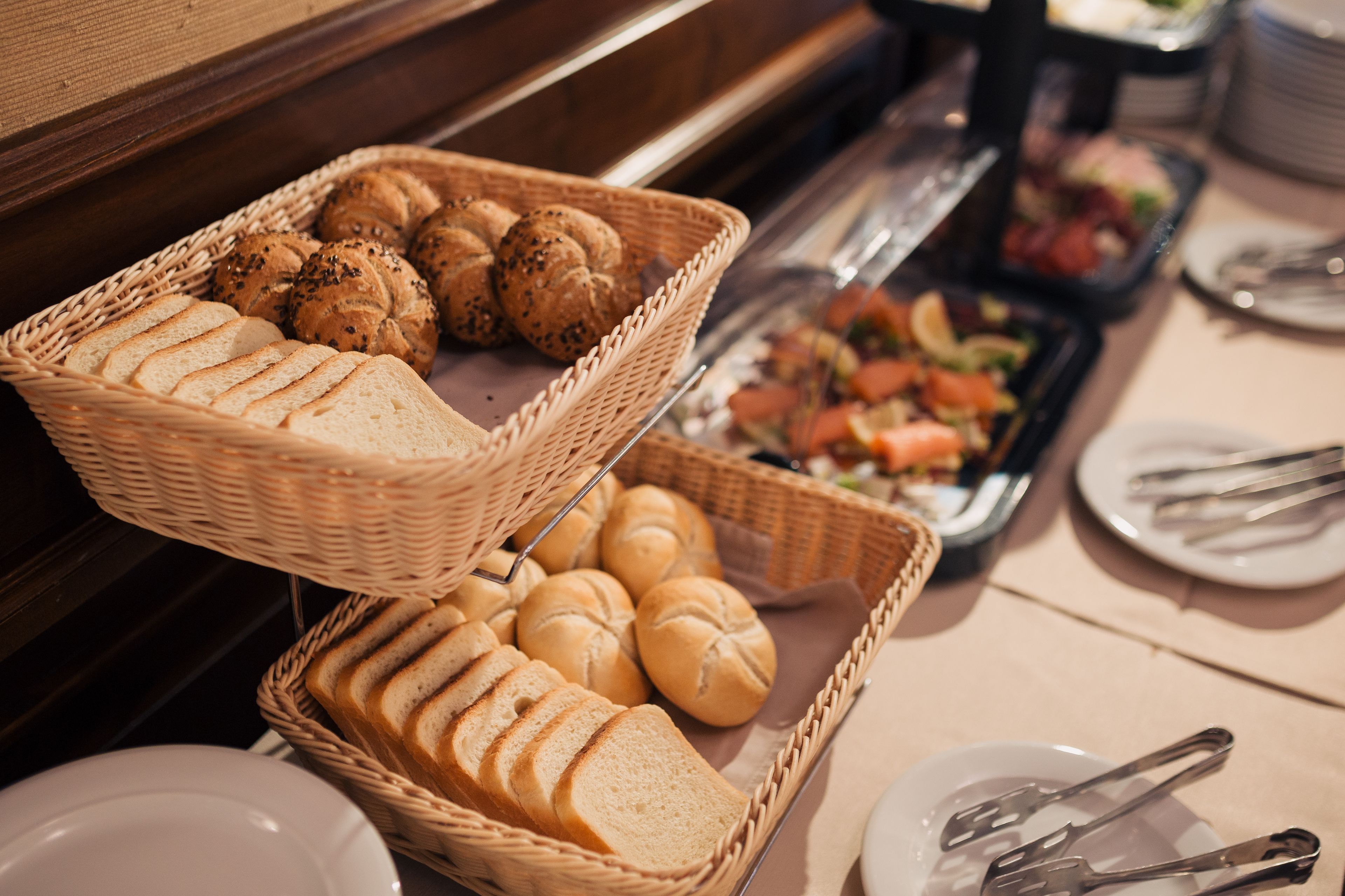 A buffet table with baskets of bread and rolls, and a tray of assorted foods.