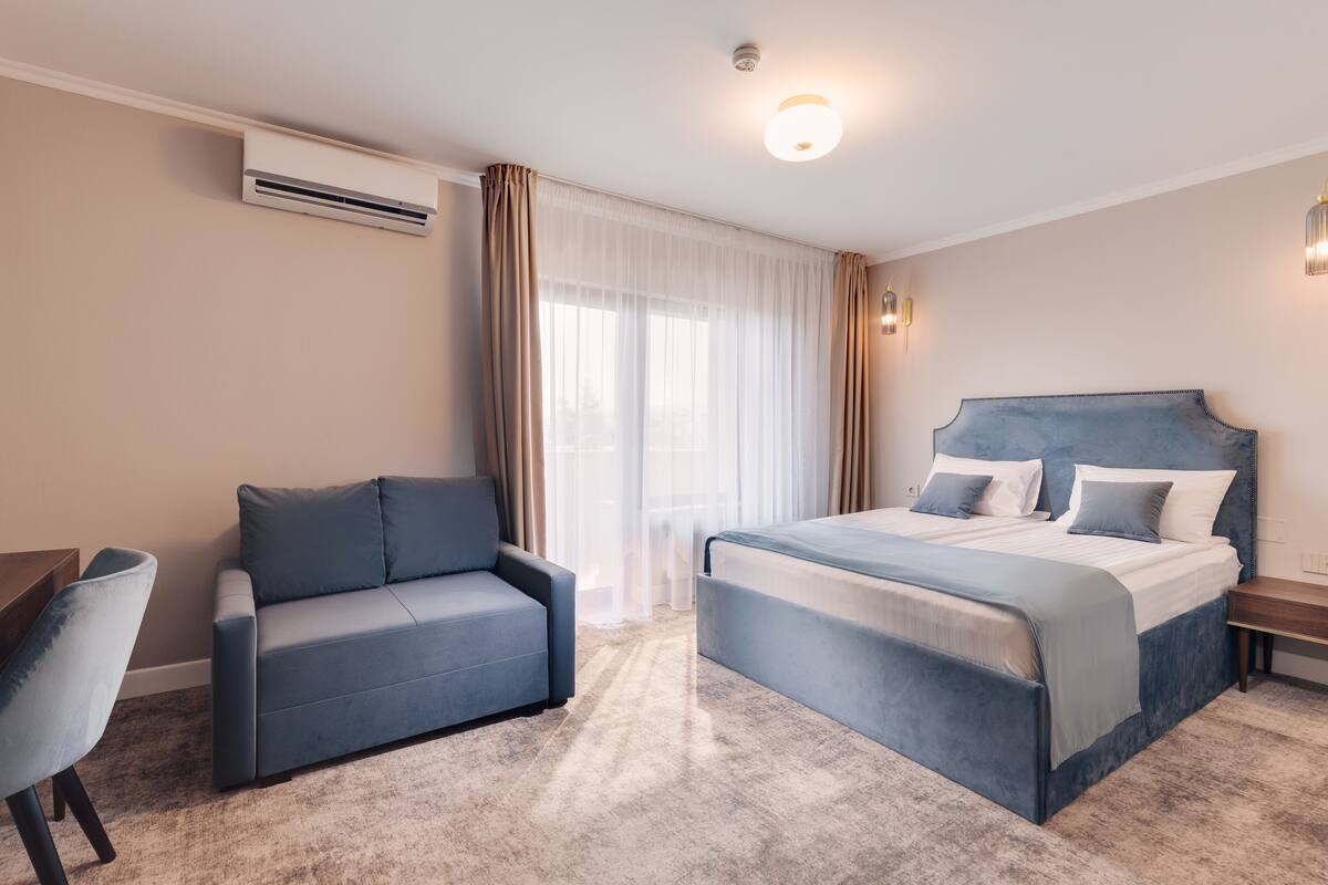 Una habitación de hotel con cama, sofá, escritorio y ventana con cortinas.