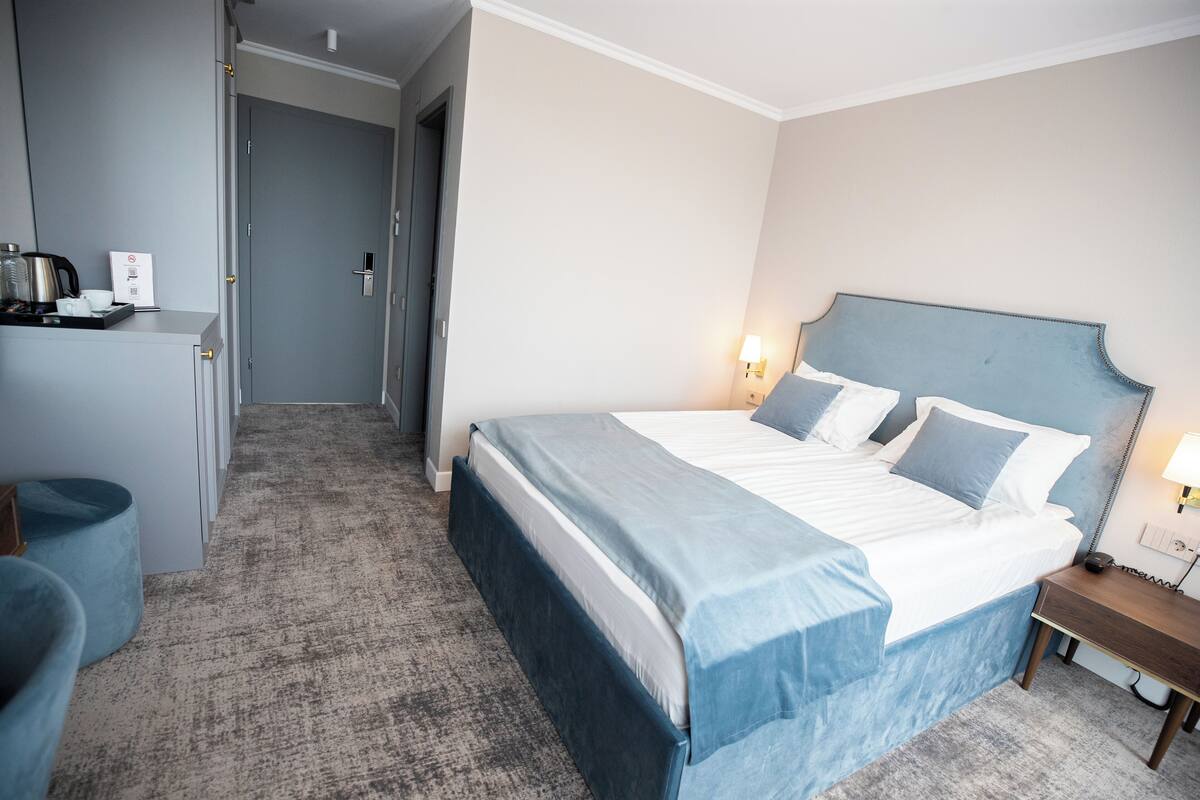 Una habitación de hotel con una cama grande, mesitas de noche, un escritorio con silla y un pequeño rincón de descanso.