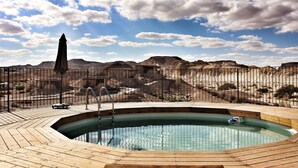 A swimming pool with a wooden deck, surrounded by a fence, and a desert landscape in the background.