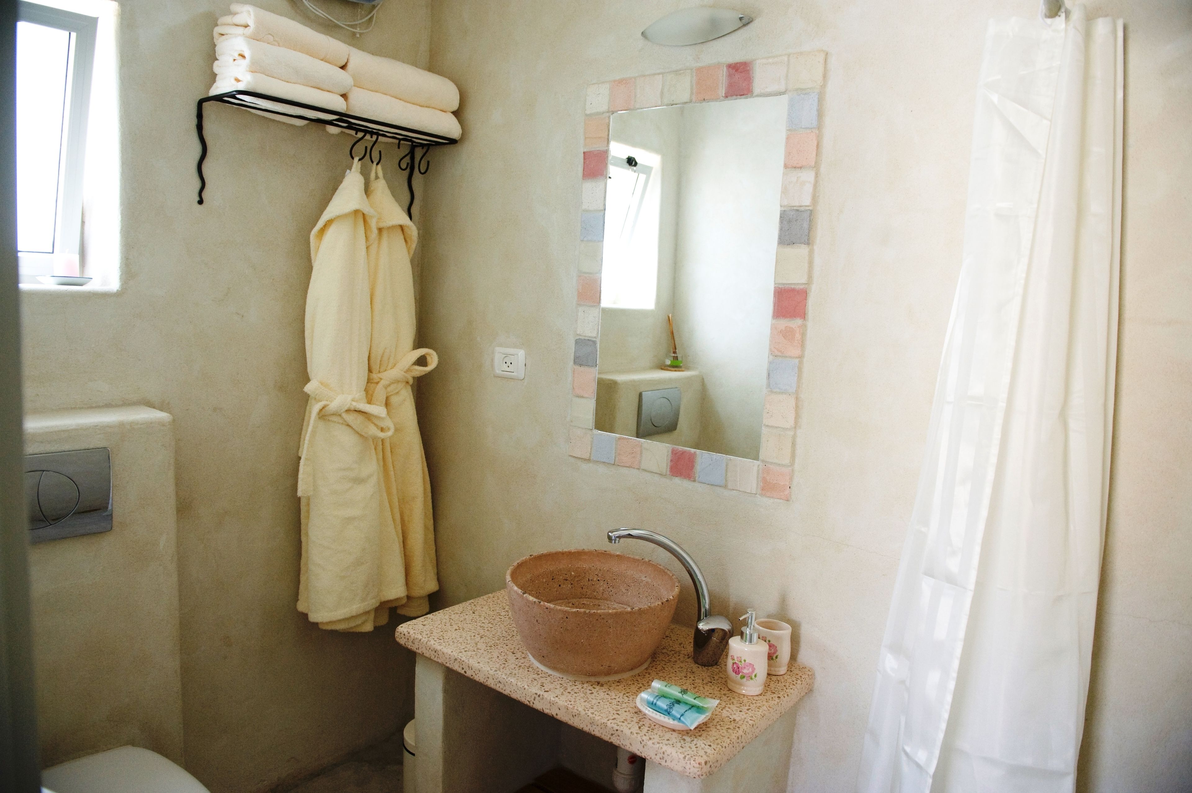 Une salle de bain avec un lavabo beige, un porte-serviettes avec des serviettes, un miroir avec un cadre coloré et un rideau de douche.