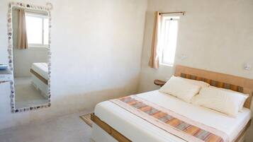 Un dormitorio con cama, espejo, ventana y mesita de noche.