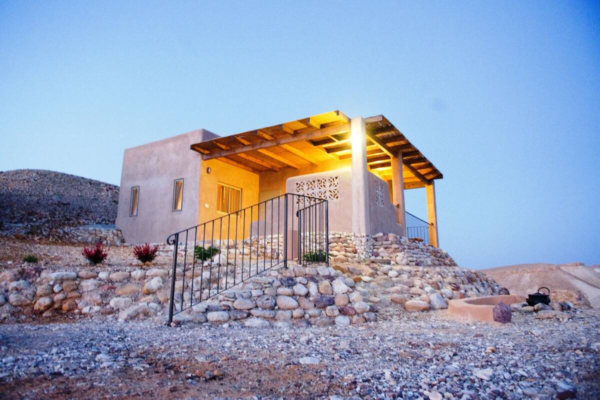 Une maison moderne avec une façade en pierre, une pergola en bois et un escalier menant à l’entrée.