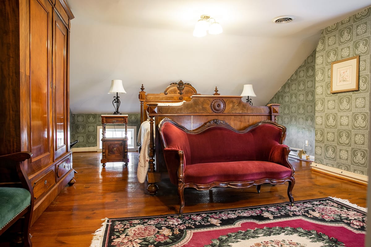 A room with a wooden wardrobe, a red sofa, a wooden bed with a headboard, and a patterned wall.