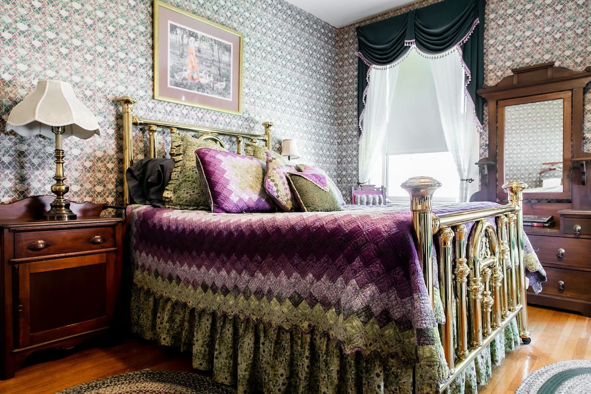 A classic bedroom with a four-poster bed, a wooden nightstand, a dresser, and a mirror.