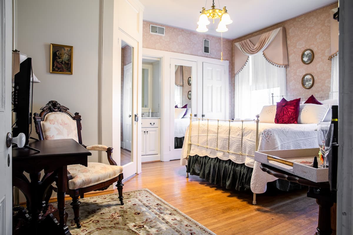 A bedroom with a bed, a chair, a desk, and a mirror.