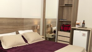A hotel room with a bed, a desk, a minibar, and a wardrobe.