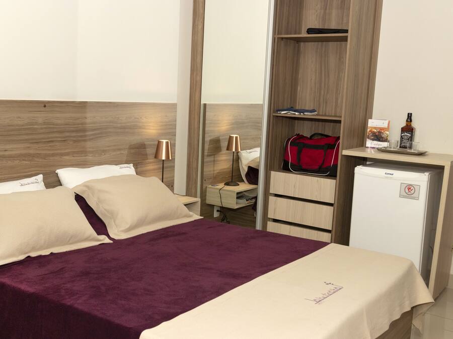 A hotel room with a bed, a desk, a minibar, and a wardrobe.