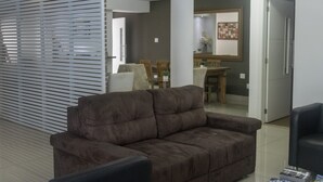 A living room with a brown sofa, a dining area with wooden furniture, and a kitchen visible through an open doorway.