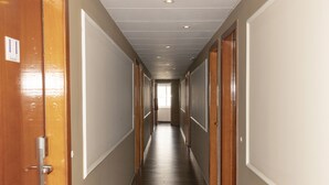 A long, narrow hallway with wooden doors on both sides, leading to a bright room at the end.