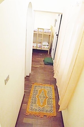 Ein schmaler Flur mit Teppichmuster, einer hölzernen Bank und einem Bett mit floralem Überwurf.