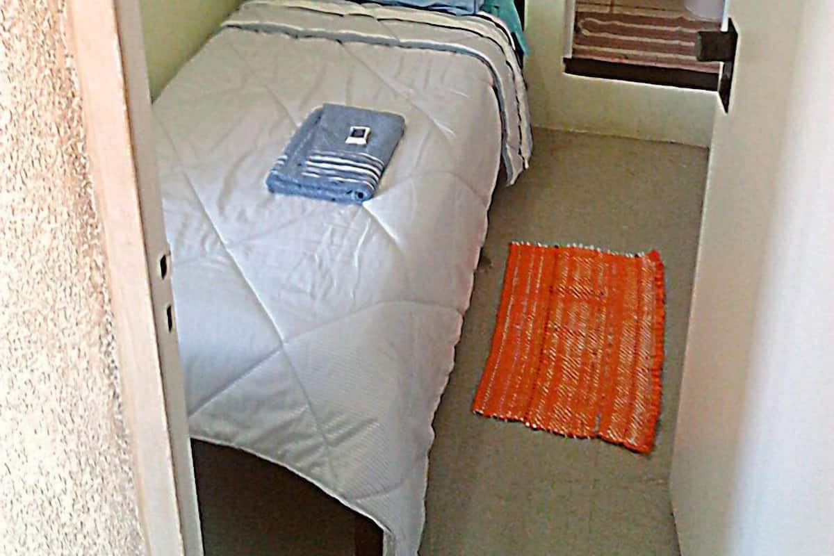 A small, narrow room with a single bed, a window, and a toilet.