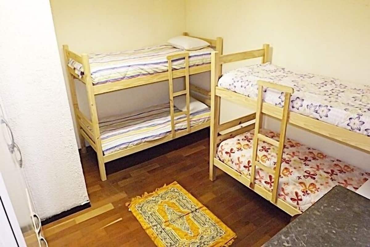 A small, compact room with two bunk beds, a wooden floor, and a patterned rug.