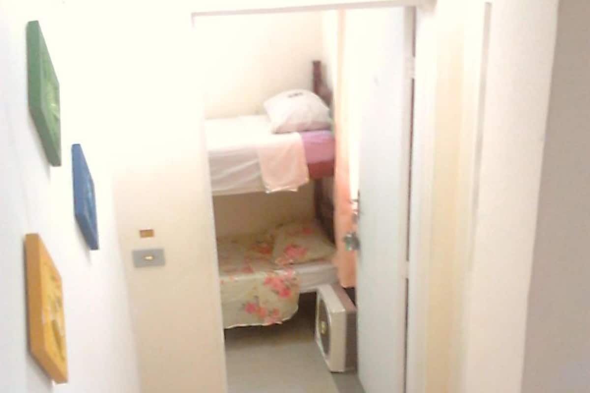 A narrow hallway leading to a bedroom with a bed, a radiator, and a door.