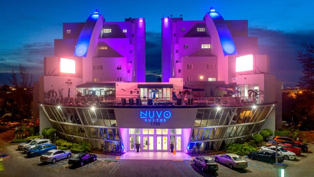 Un hôtel au design moderne, doté d'une entrée imposante avec une enseigne lumineuse au néon, de nombreux espaces de stationnement et d'une façade bien éclairée.
