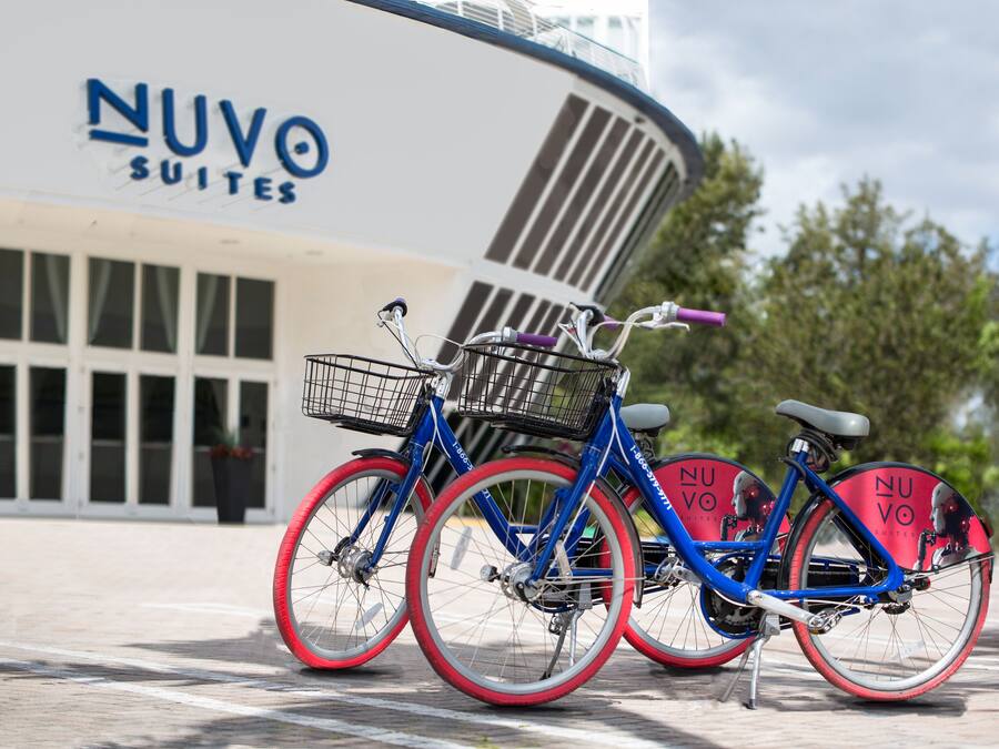 Zwei Fahrräder mit roten Reifen stehen vor einem Gebäude, an dem ein Schild mit der Aufschrift "NUVO SUITES" angebracht ist.