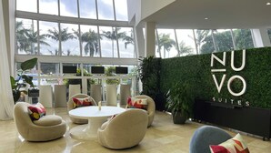 Un hall d’hôtel moderne, doté de sièges confortables, de grandes fenêtres et d’une enseigne indiquant « NUVO SUITES ».