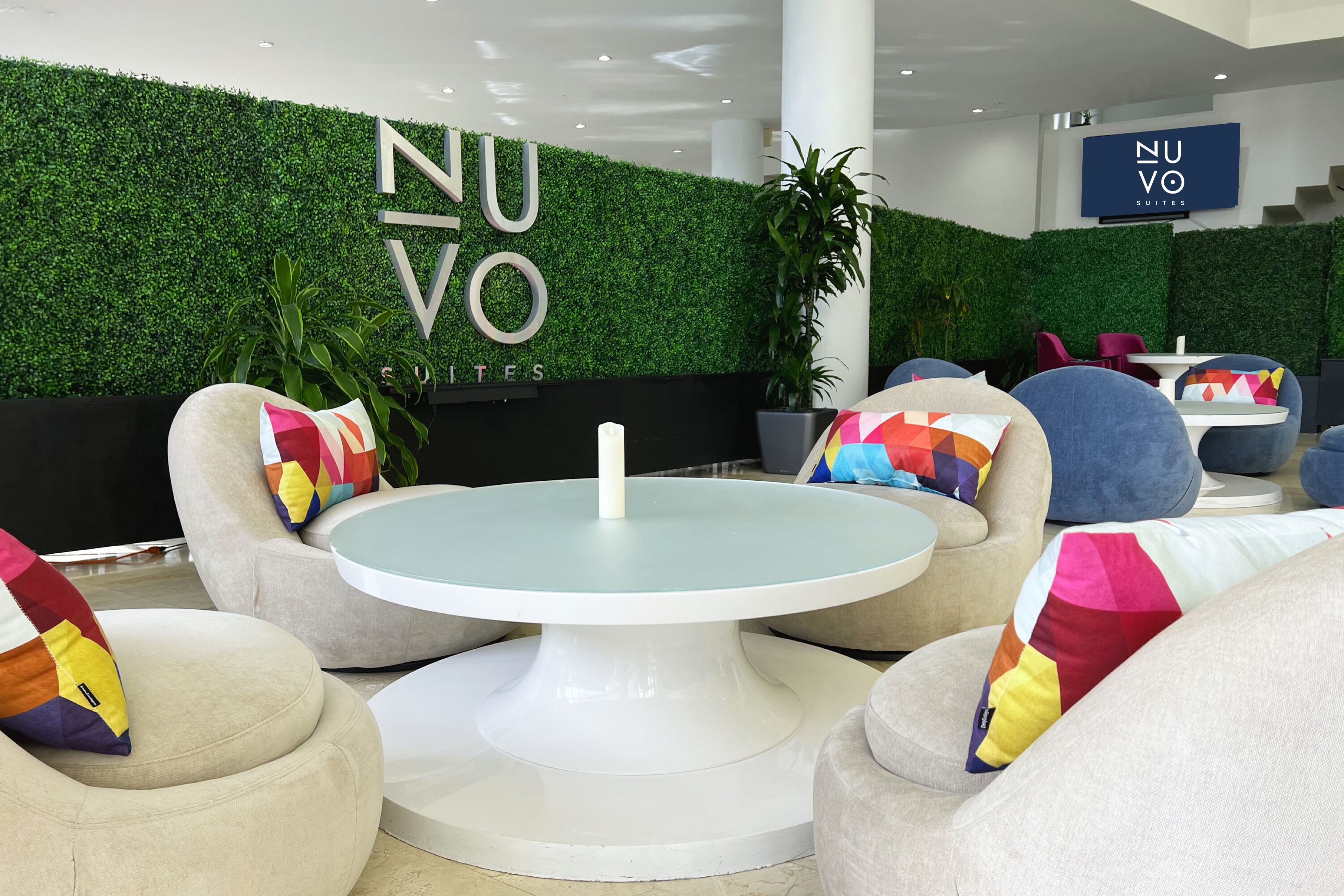 A modern hotel lobby with a green wall, comfortable seating, and a sign reading "NUVO SUITES".