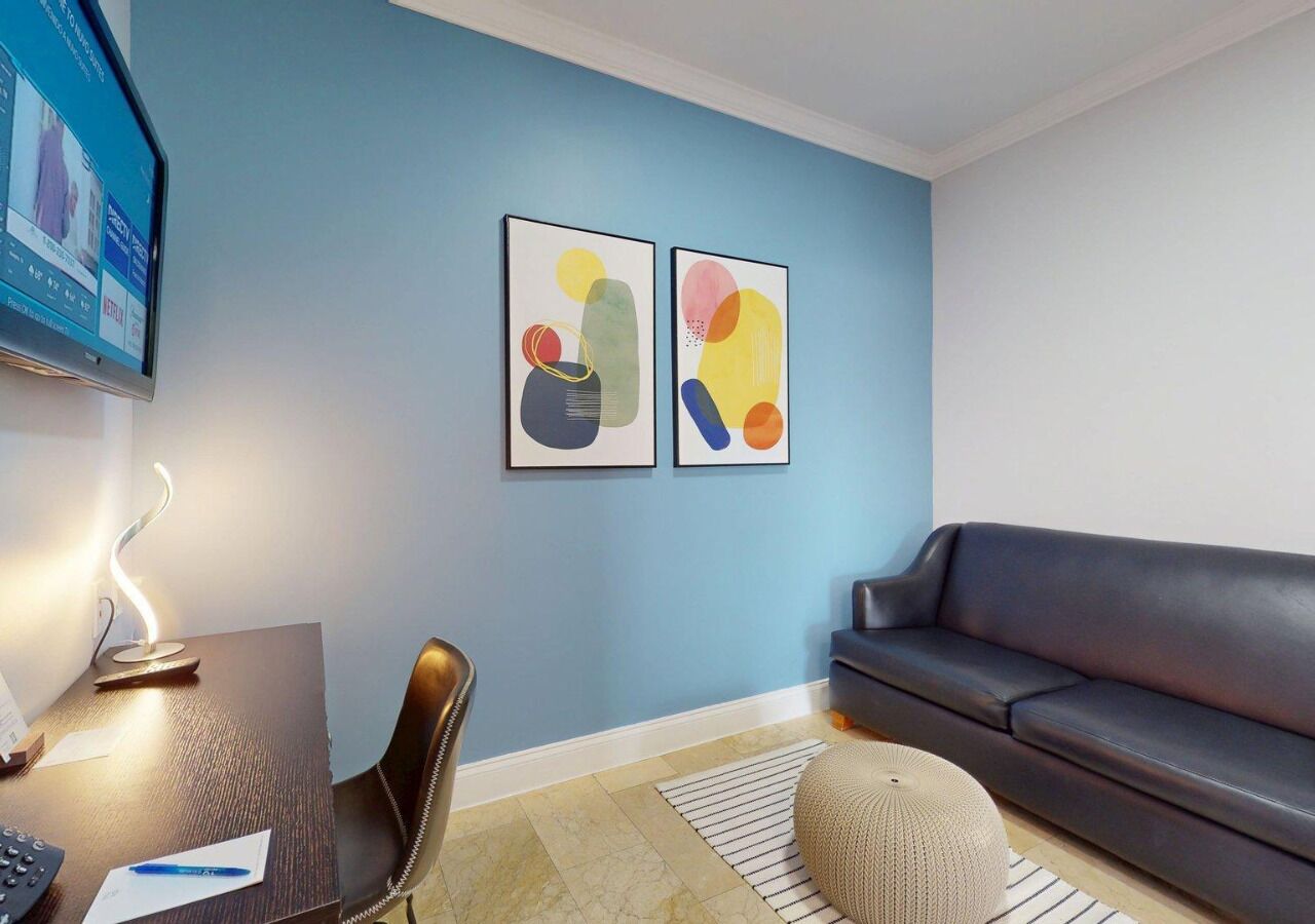 A modern living room with a dark sofa, a desk with a computer, and two abstract paintings on the wall.