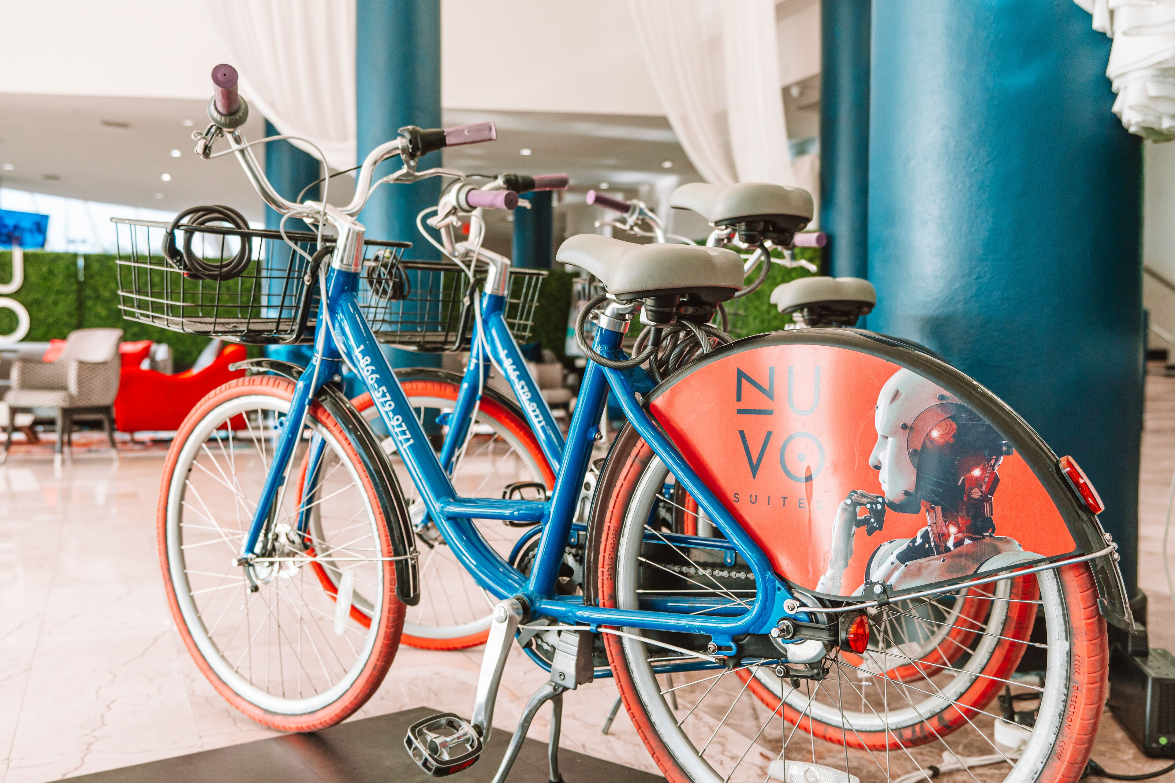 A blue bicycle with a basket and a red and white seat, parked indoors.