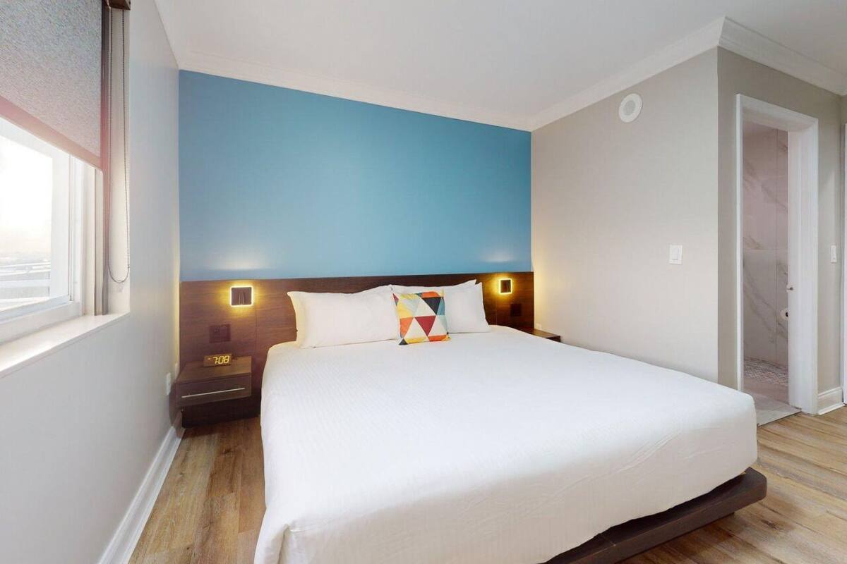 A bedroom with a large bed, a nightstand with a clock, and a wall-mounted light.