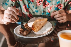 Une personne tenant une fourchette et mangeant dans une assiette, avec une pâtisserie et des boulettes de viande.