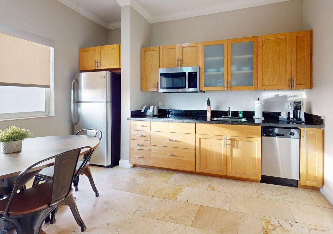 A modern kitchen with wooden cabinets, stainless steel appliances, a dining table with chairs, and a potted plant.