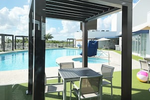 A pool area with a covered seating area, a slide, and a building in the background.