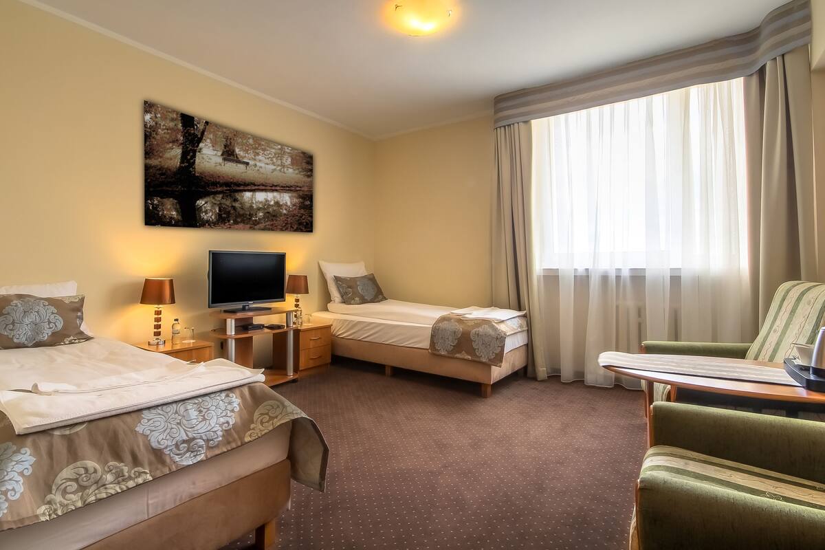 A hotel room with two beds, a TV, a desk with a lamp, and a chair.