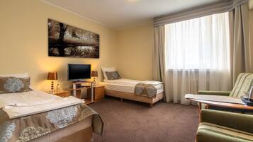 Ein Hotelzimmer mit zwei Betten, einem Fernseher, einem Schreibtisch mit Lampe und einem Sessel.