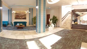 A hotel lobby with a reception desk, a staircase, a blue sofa, and a coffee table. - Confero (Nysa)