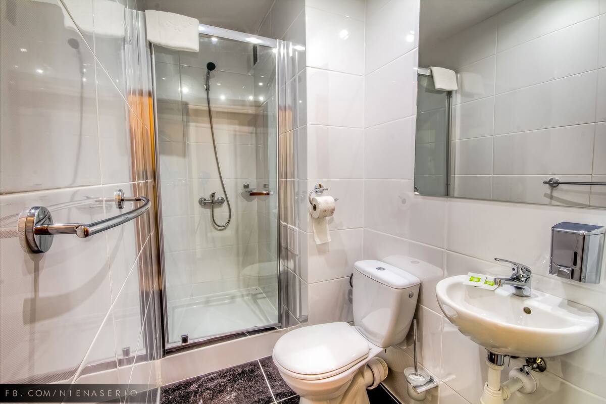 A modern bathroom with a glass-enclosed shower, a white toilet, and a sink with a soap dispenser.
